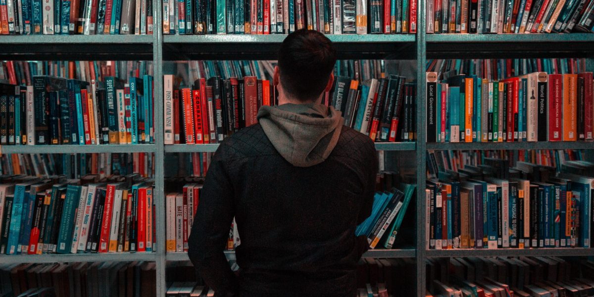 Man standing in front of library shelves, back profile